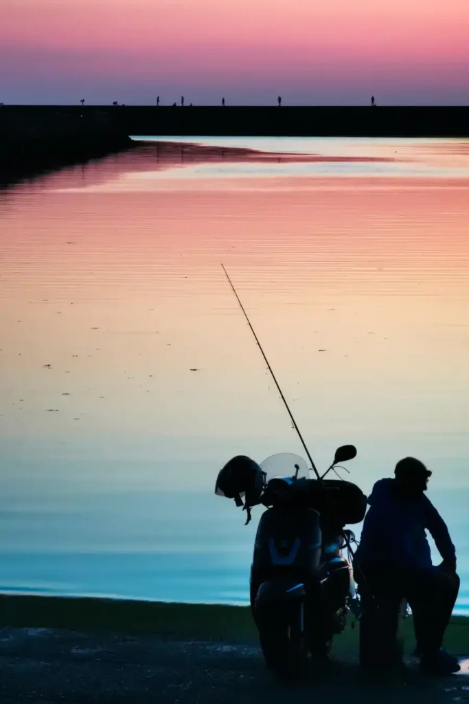 Le ciel rose et violet d'un couché de soleil et le reflet au couleur de l'arc en ciel dans l'eau. Un pêcheur a moto pour observer le paysage. 16° Lauréat du concours photo WinSPOT by Data Concept