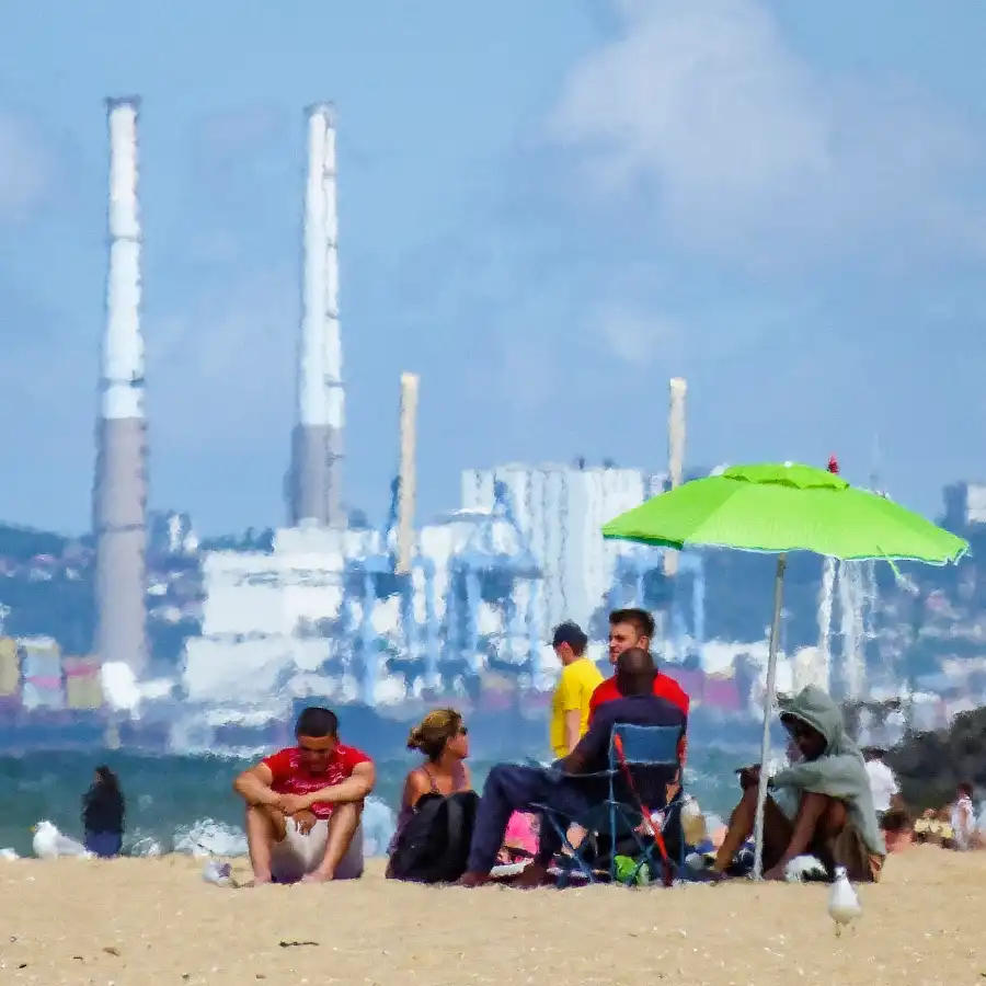 Des hommes et des femmes sous un parasol sur la plage. Avec les cheminées du havre en fond. 6° Lauréat du concours photo WinSPOT by Data Concept